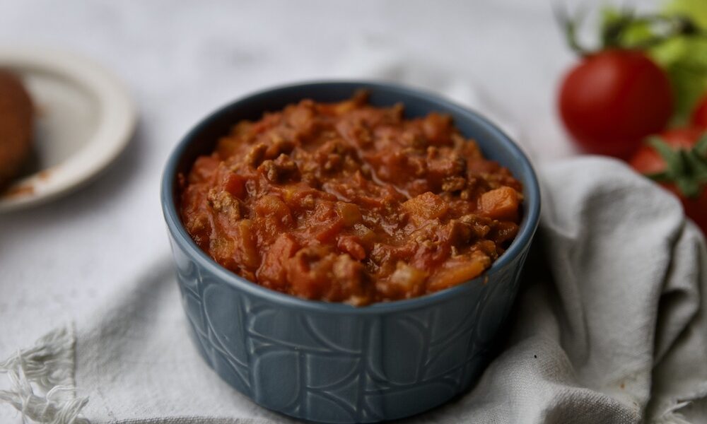 Traditional Bolognese sauce: the Italian Ragù Bowl of Bolognese sauce with a spoon and tomatoes in the background
