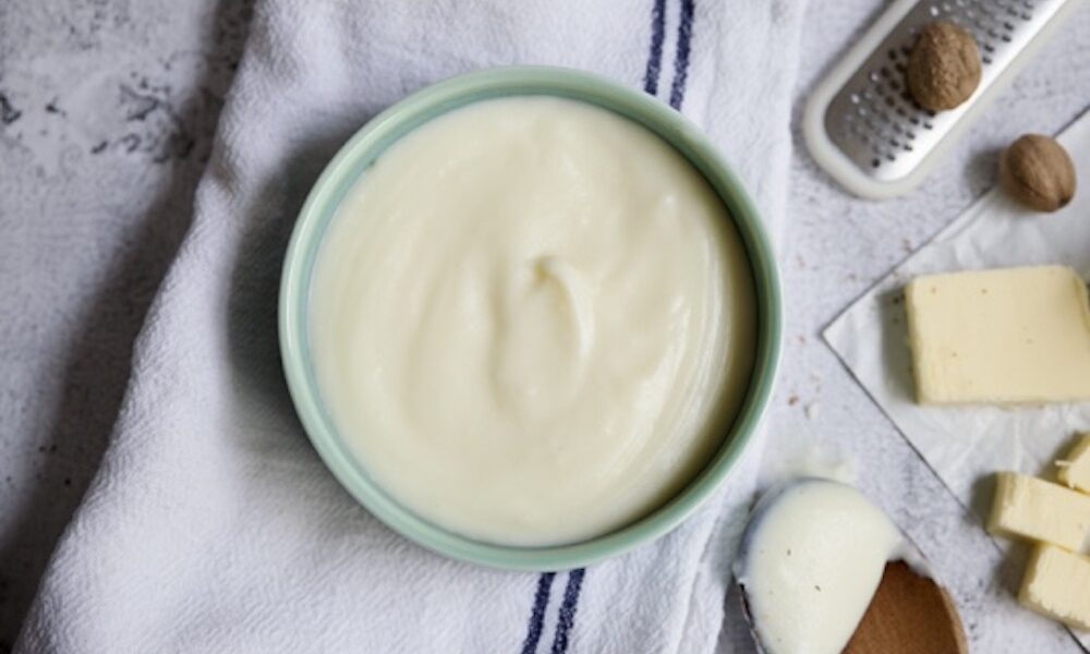 béchamel sauce in a bowl with butter and nutmeg in the background