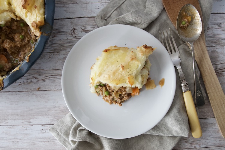 Shepherd's pie on a plate with the pie on the left and cutlery on the right